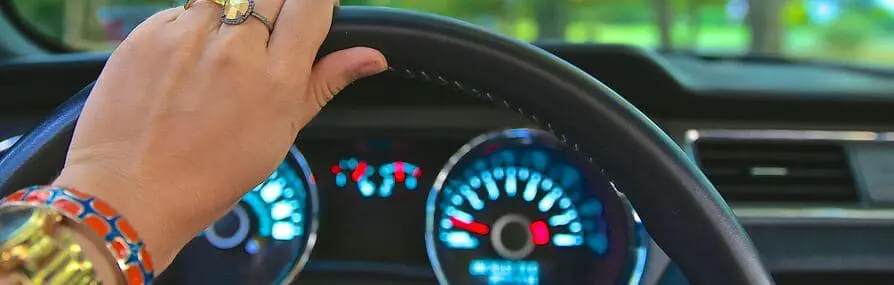Mão segurando o volante com o painel iluminado. Lembre-se de verificar as coberturas do seu seguro de carro.