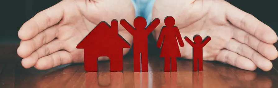 Figuras de uma família entre mãos protetoras ao lado de uma casa simbolizam seguro de lar.
