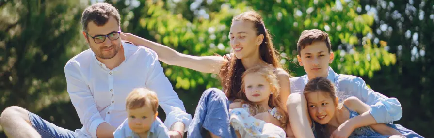 Família com seis pessoas relaxa ao ar livre discutindo sobre seguros sob céu claro.