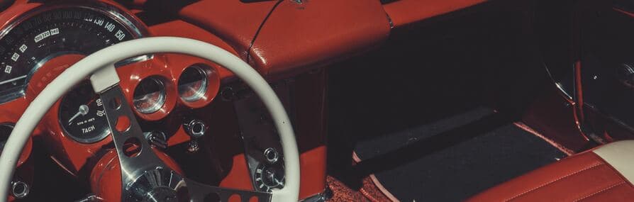 Interior de um carro clássico com painel vermelho e volante branco. Faça um seguro de veículo antigo.