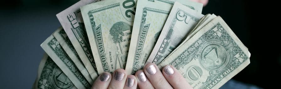 Mãos segurando várias notas de dólar ilustrando economias de seguros.