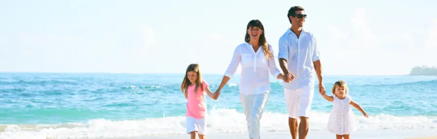 O que é um Seguro de Vida? Família sorridente caminha na praia ensolarada cobertos de seguro de viagem.